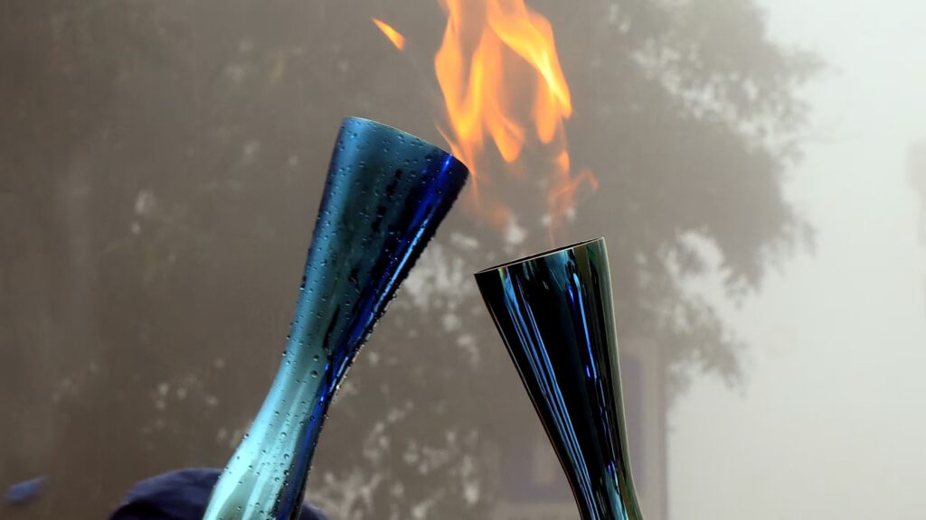 Dettaglio ravvicinato di due torce olimpiche di Milano Cortina 2026 mentre si scambiano la fiamma.